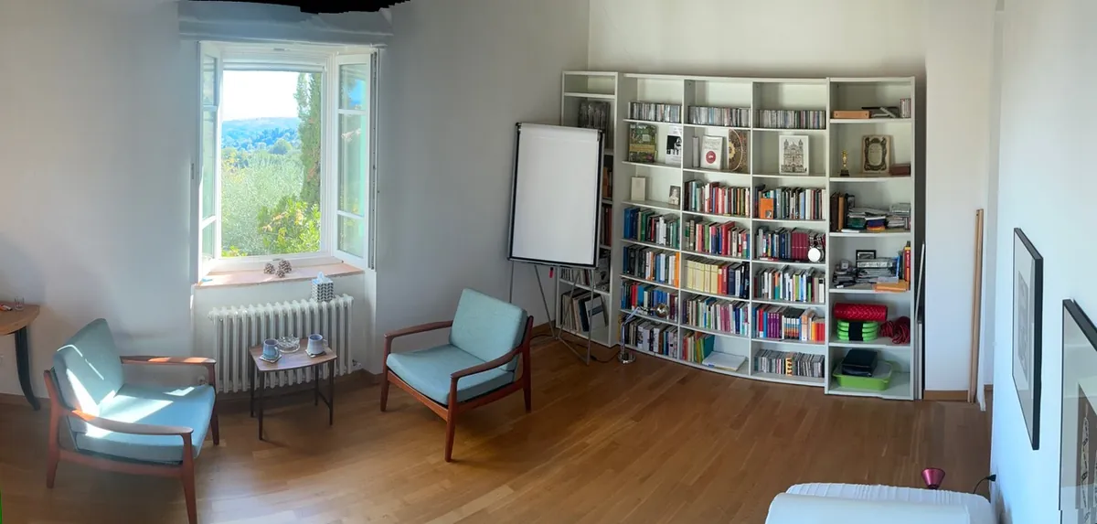 Weiter Raum mit Bücherregal, Sesseln und Fenstern